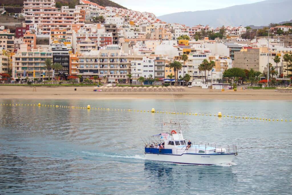 Blog 7 guía turística los cristianos tenerife - a boat traveling on the water in front of a city