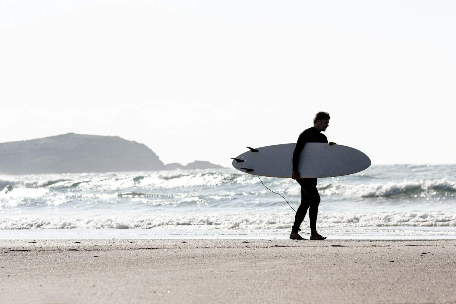 Guía de Deportes Acuáticos en Los Cristianos 1 deportes acuáticos en los cristianos - a man holding a surfboard on top of a sandy beach