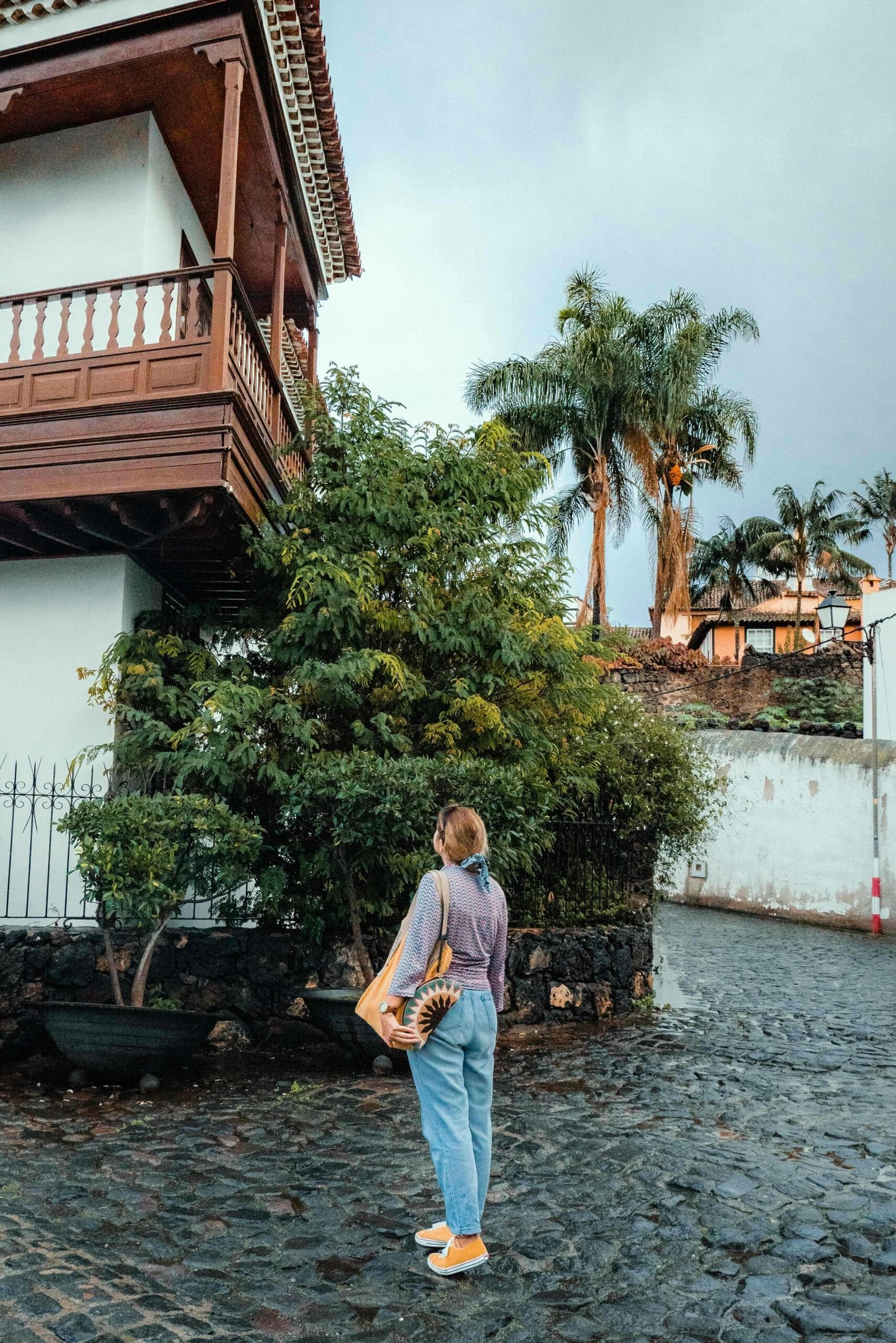 Woman walking on cobblestone street in Icod de los Vinos, Spain, near traditional wooden house.